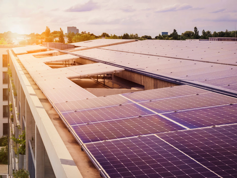 Panell solar instal·lat en un edifici amb llum del sol al fons.